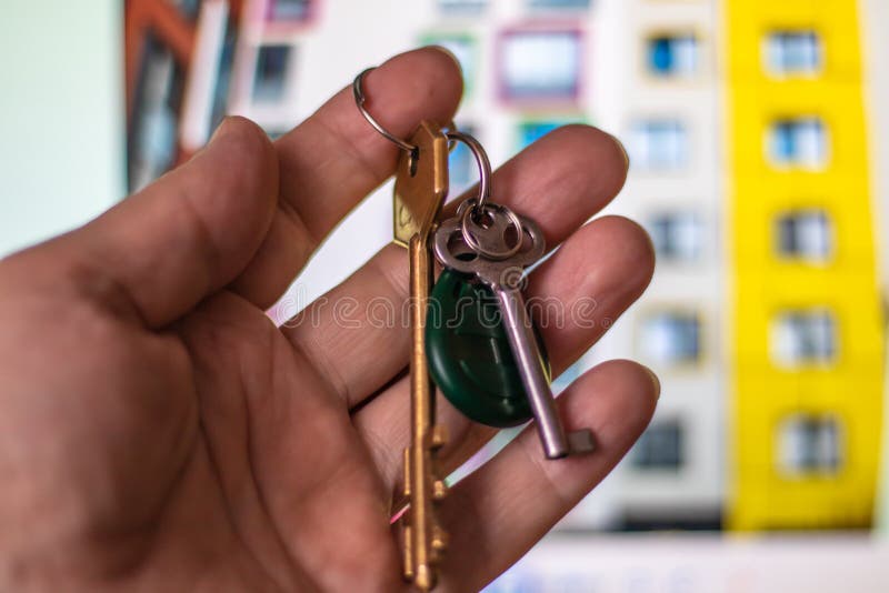 Foto del primo piano della mano di un uomo che tiene le chiavi ad una nuova casa sui precedenti di un edificio residenziale moder fotografie stock libere da diritti Foto del primo piano della mano di un uomo che tiene le chiavi ad una nuova casa sui precedenti di un edificio residenziale moder fotografie stock libere da diritti