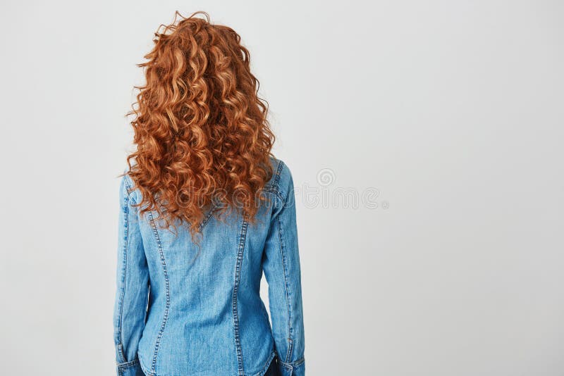 Foto della ragazza con capelli ricci rossi che stanno di nuovo alla macchina fotografica sopra fondo bianco Copi lo spazio