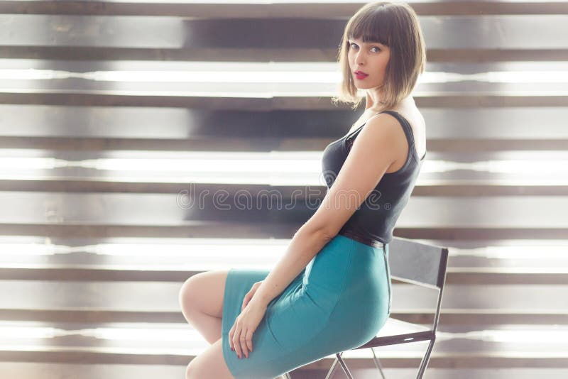 Foto des jungen Brunette sitzend auf Stuhl nahe Fenster mit Vorhängen lizenzfreie stockfotografie Foto des jungen Brunette sitzend auf Stuhl nahe Fenster mit Vorhängen lizenzfreie stockfotografie