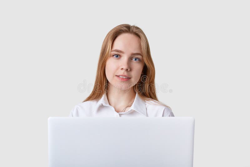 Foto di giovane donna allegra caucasica che si siede sopra la parete bianca con il computer lportable del aptop Esaminando dirett fotografia stock Foto di giovane donna allegra caucasica che si siede sopra la parete bianca con il computer lportable del aptop Esaminando dirett fotografia stock