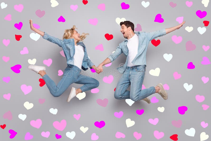 Foto di una coppia di innamorati ispirati salti per mano indossate jeans casuali vestite di sfondo grigio isolato immagini stock