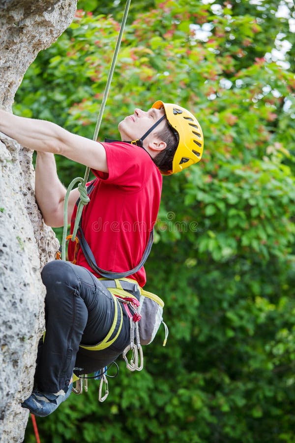 Foto do desportista no capacete amarelo que escala sobre a rocha contra o fundo de árvores verdes imagem de stock Foto do desportista no capacete amarelo que escala sobre a rocha contra o fundo de árvores verdes imagem de stock