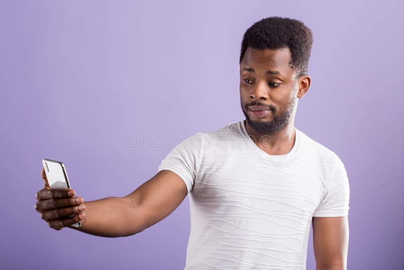 Foto do homem negro confundido surpreendido que guarda o telefone celular moderno foto de stock royalty free Foto do homem negro confundido surpreendido que guarda o telefone celular moderno foto de stock royalty free