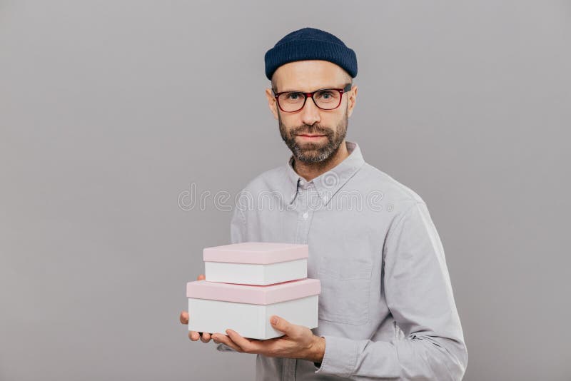 A foto do modelo masculino sério vestido na roupa festiva, guarda presentes nas mãos, indo felicitar o amigo com o aniversário, p imagem de stock A foto do modelo masculino sério vestido na roupa festiva, guarda presentes nas mãos, indo felicitar o amigo com o aniversário, p imagem de stock