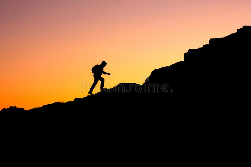 Photo in a dark key of a man climbing a mountain. a man illuminated from behind by the sun climbs up the mountain. Photo in a dark key of a man climbing a mountain. a man illuminated from behind by the sun climbs up the mountain