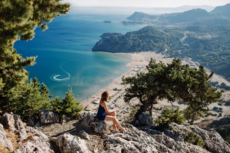 Foto einer Meereslandschaft, Blick auf die Bucht von Tsambika auf der Insel Rhodos Mädchen sitzt auf einem Stein und blickt auf e stockbilder
