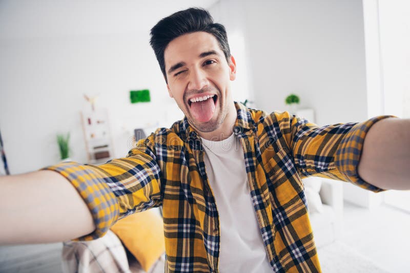 Photo of funky positive man wear checkered shirt stick out tacking selfie indoors house apartment room. Photo of funky positive man wear checkered shirt stick out tacking selfie indoors house apartment room.