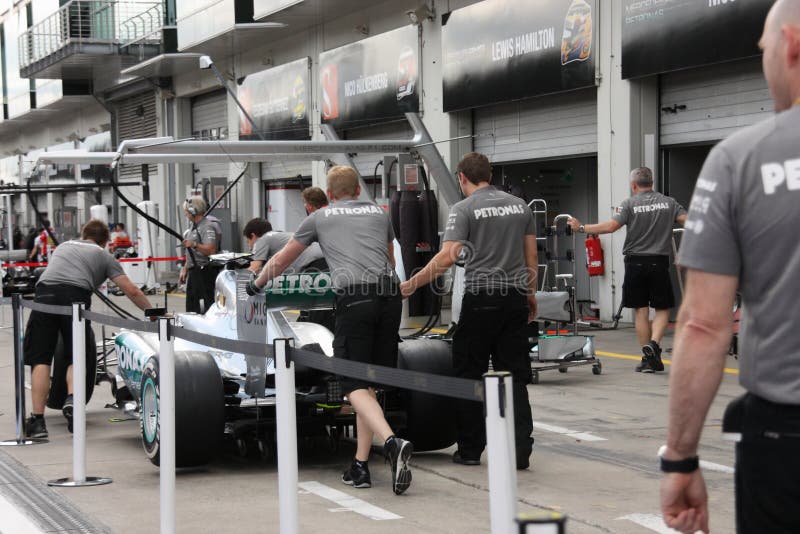 F1 Photo - Formula 1 Mercedes car in paddock : team mechanics push the racing car to the boxes. F1 Photo - Formula 1 Mercedes car in paddock : team mechanics push the racing car to the boxes