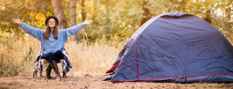 Foto in formato banner di una turista di campeggio con le mani in alto in maglione e cappello nero che si alza nella tenda del cam