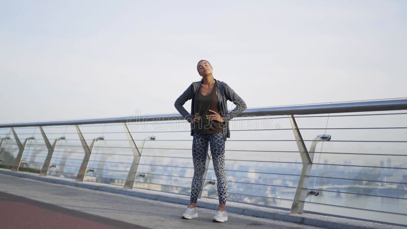 Foto longa extra. garota atleta africana fica na ponte e faz exercícios para o pescoço e o ombro