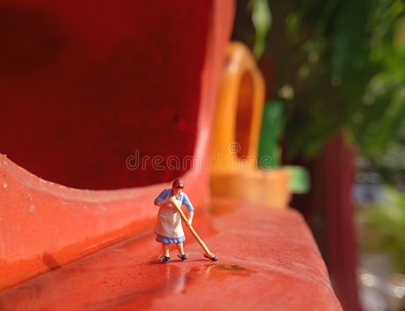 Foto Mini figura giocattolo donna che pulisce l'acqua rovesciata nel cestino della plastica arancione fotografia stock
