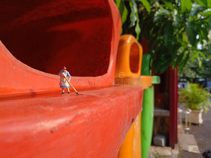 Foto Mini figura giocattolo donna che pulisce l'acqua rovesciata nel cestino della plastica arancione fotografie stock libere da diritti