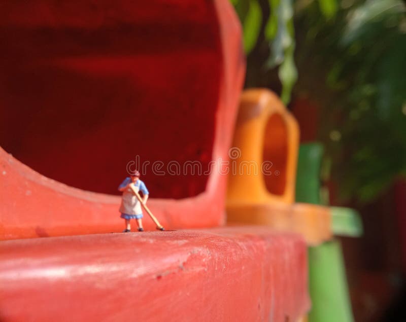 Foto Mini figura giocattolo donna che pulisce l'acqua rovesciata nel cestino della plastica arancione fotografia stock