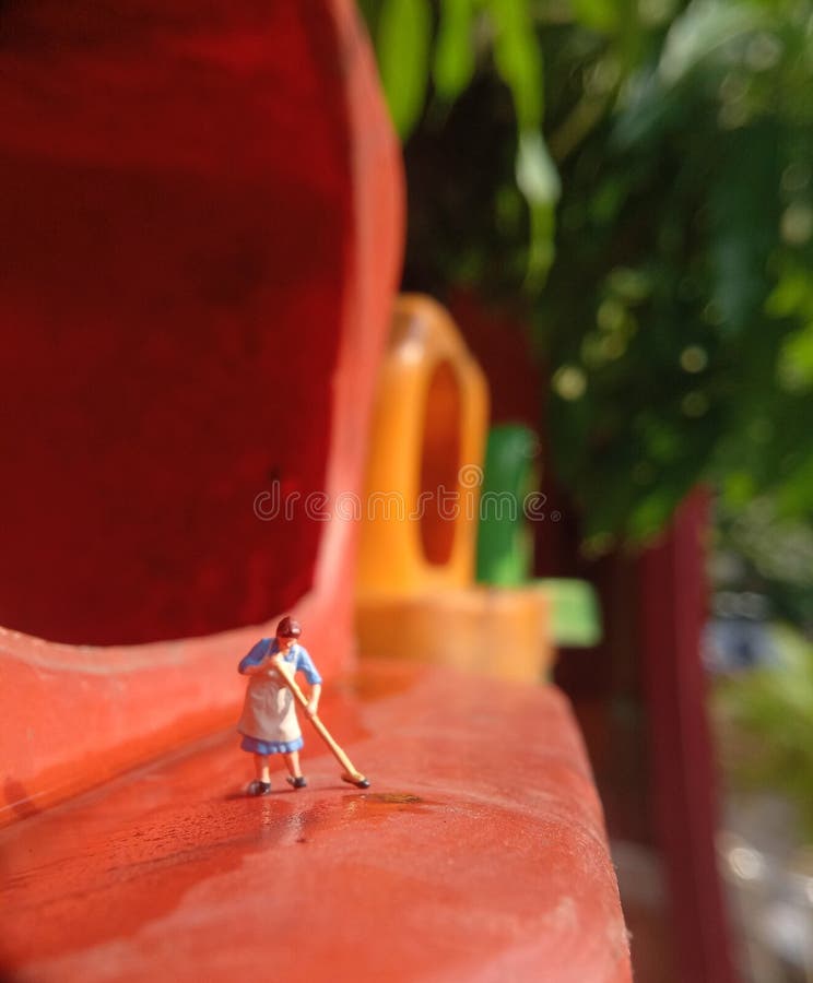 Foto Mini figura giocattolo donna che pulisce l'acqua rovesciata nel cestino della plastica arancione fotografie stock libere da diritti