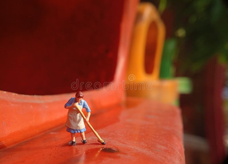 Foto Mini figura giocattolo donna che pulisce l'acqua rovesciata nel cestino della plastica arancione immagini stock
