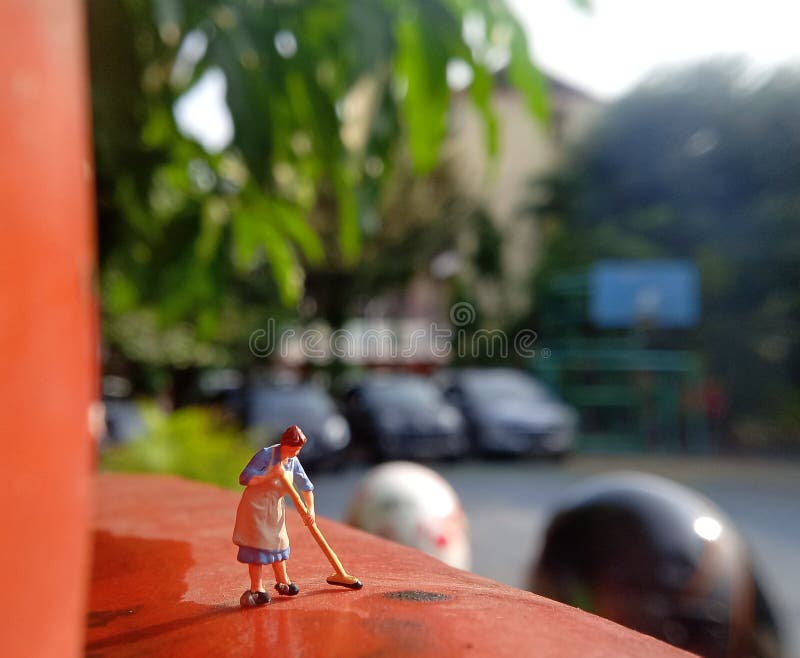 Foto Mini figura giocattolo donna che pulisce l'acqua rovesciata nel cestino della plastica arancione fotografia stock libera da diritti