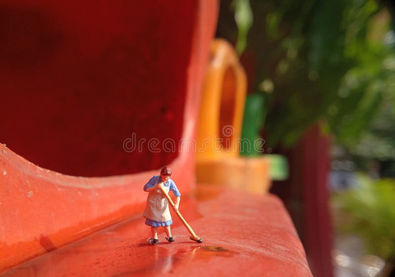 Foto Mini figura giocattolo donna che pulisce l'acqua rovesciata nel cestino della plastica arancione immagini stock