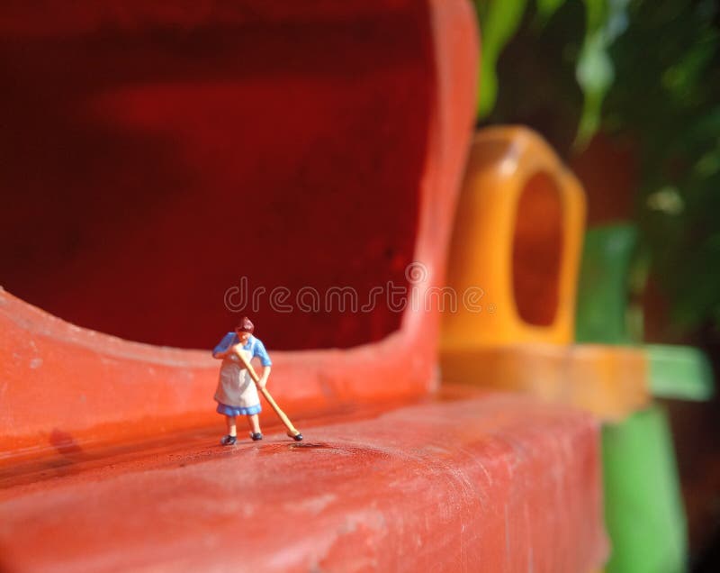 Foto Mini figura giocattolo donna che pulisce l'acqua rovesciata nel cestino della plastica arancione fotografie stock libere da diritti