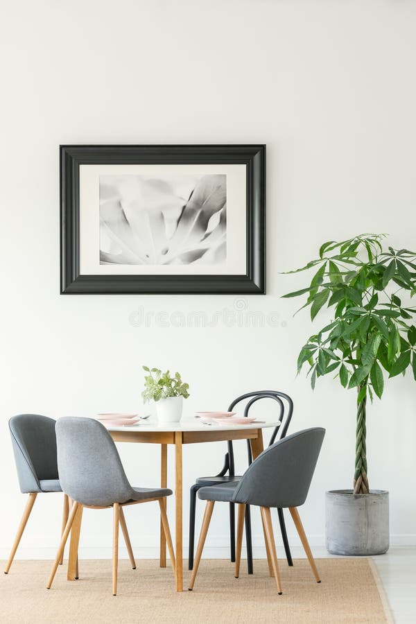Foto real de un interior del comedor con una tabla, las sillas, el árbol y la pintura en un marco negro imagen de archivo libre de regalías Foto real de un interior del comedor con una tabla, las sillas, el árbol y la pintura en un marco negro imagen de archivo libre de regalías