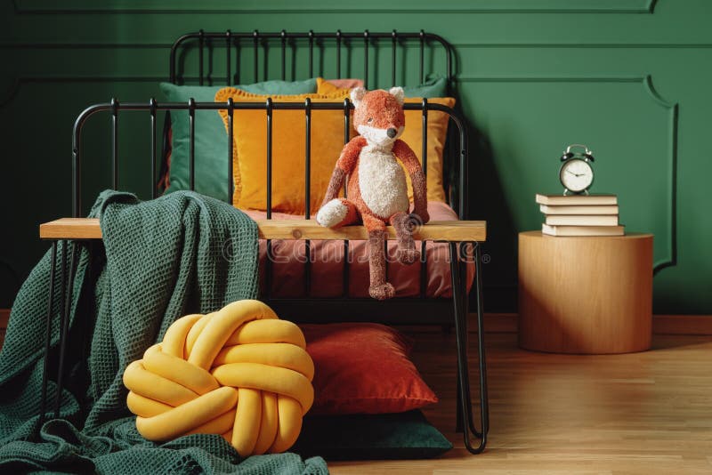 Foto real de una almohada del nudo, de una manta verde y de un zorro de la felpa en un banco de madera delante de una cama negra fotos de archivo Foto real de una almohada del nudo, de una manta verde y de un zorro de la felpa en un banco de madera delante de una cama negra fotos de archivo