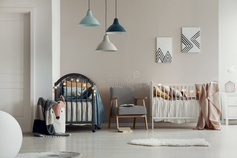 Foto reale di una camera spaziosa, bianca e beige all'interno per due gemelli con due costole di legno e una poltrona fotografie stock libere da diritti