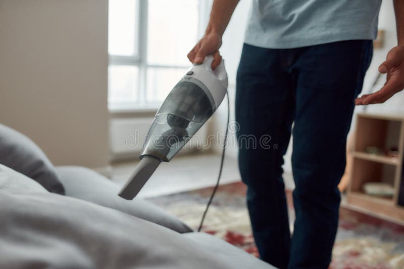 Foto recortada de um sofá de limpeza de homem com vácuo de mão enquanto trabalhava na sala de estar fotografia de stock royalty free