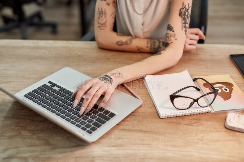 Foto recortada de uma mulher tatuada digitando algo no laptop enquanto trabalhava no escritório imagens de stock