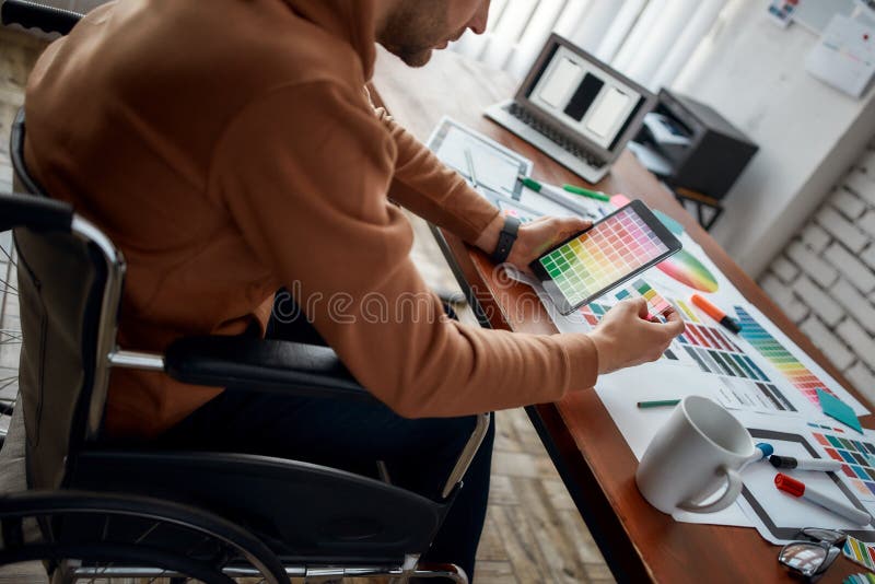 Foto recortada do desenhador ui masculino do ux numa cadeira de rodas que seleciona as cores certas para o aplicativo móvel enquan foto de stock