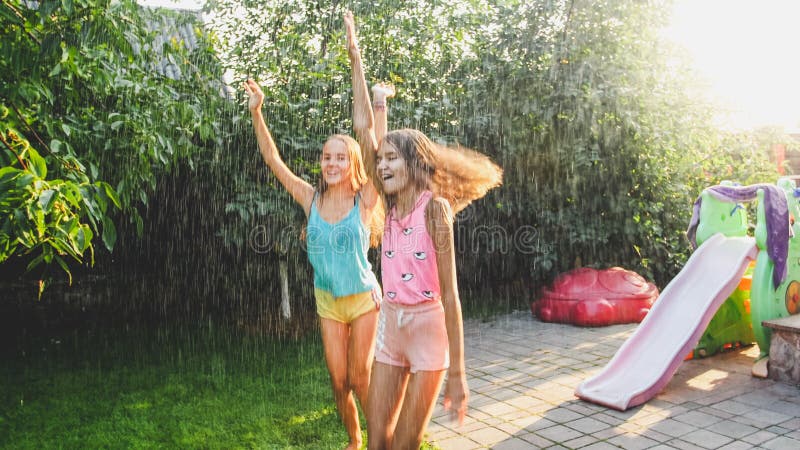 Foto van twee gelukkige lachende zusters in natte kleren die onder waterdruppeltjes van tuinslang bij tuin dansen Familie royalty-vrije stock afbeeldingen Foto van twee gelukkige lachende zusters in natte kleren die onder waterdruppeltjes van tuinslang bij tuin dansen Familie royalty-vrije stock afbeeldingen