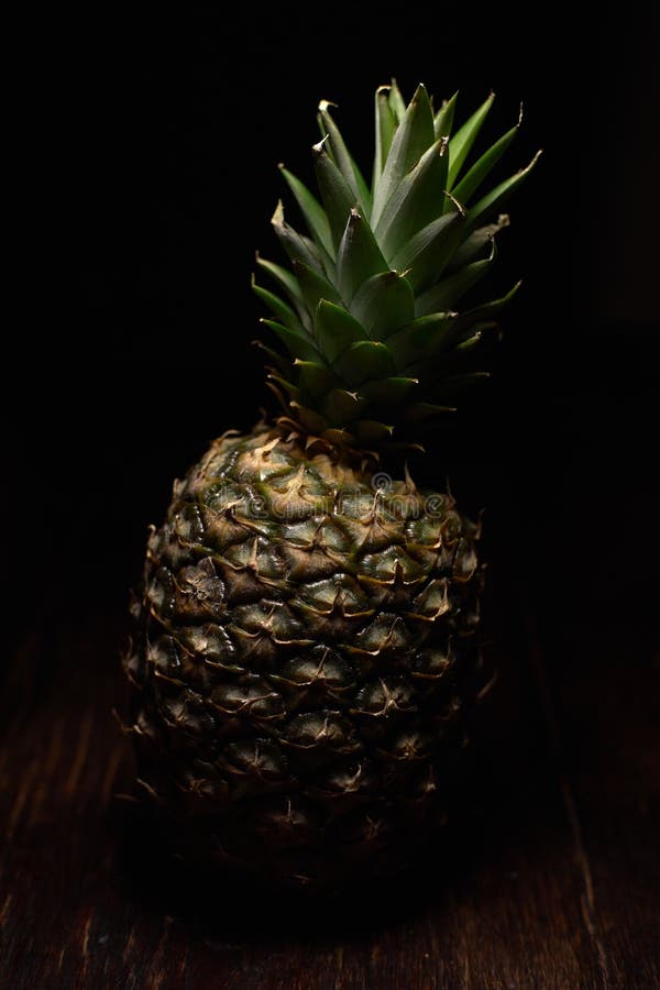 Foto verticale di un ananas su una superficie di legno con fondo nero immagini stock libere da diritti Foto verticale di un ananas su una superficie di legno con fondo nero immagini stock libere da diritti