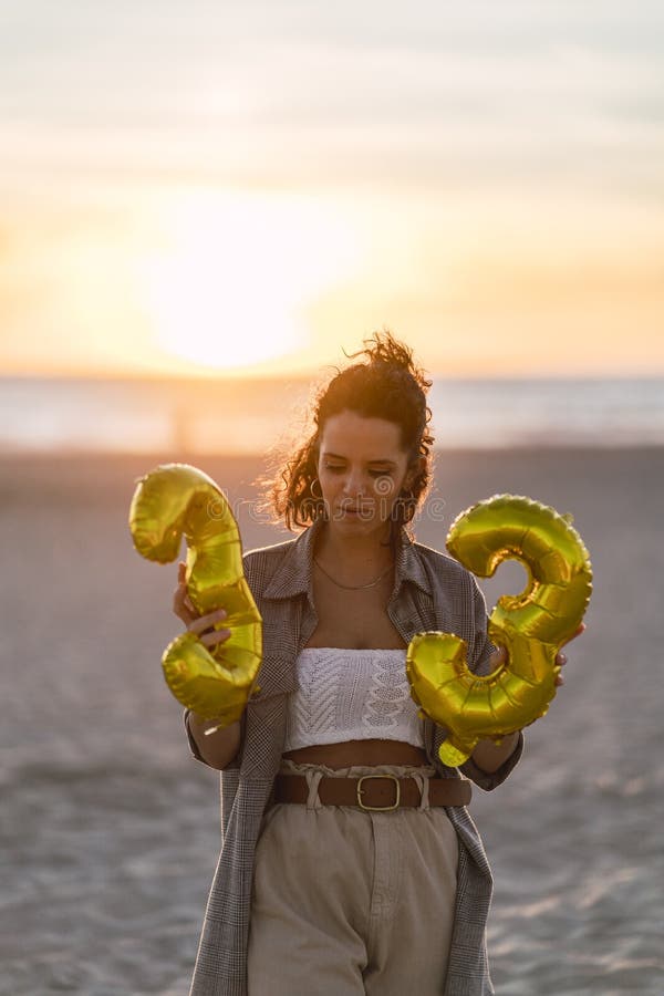 Foto verticale di una giovane modella che posava su una spiaggia con palloncini per il suo 33esimo compleanno immagine stock libera da diritti