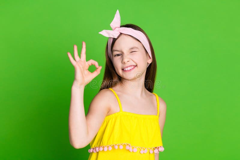 Photo of charming cute small girl wear yellow dress wink eye showing okey sign empty space isolated green color background. Photo of charming cute small girl wear yellow dress wink eye showing okey sign empty space isolated green color background.