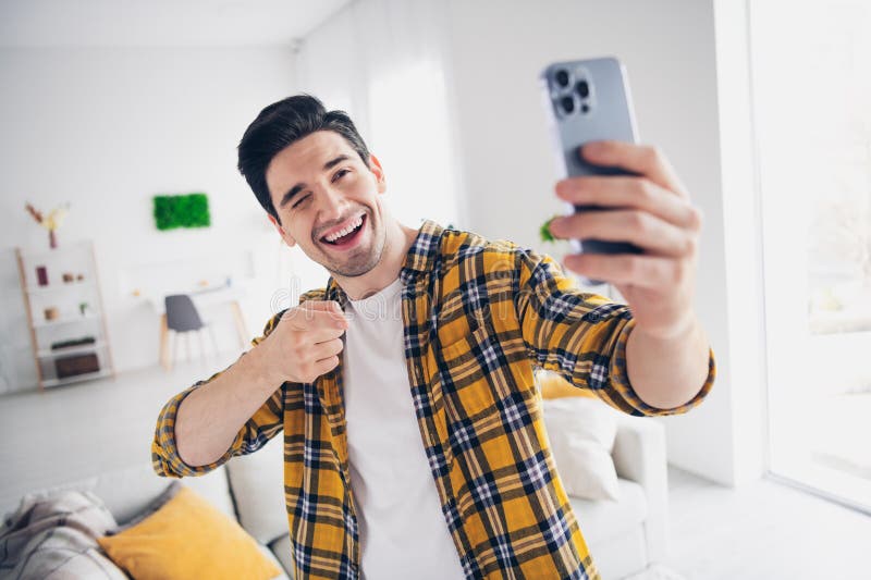 Photo of cool good mood man wear checkered shirt tacking selfie pointing finger modern device indoors house apartment room. Photo of cool good mood man wear checkered shirt tacking selfie pointing finger modern device indoors house apartment room.