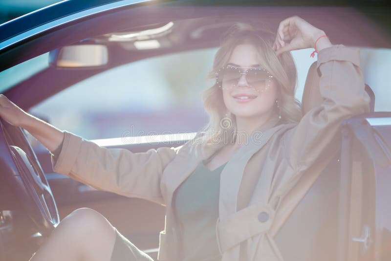 Foto von jungen Blondinen mit den Gläsern und langem Kleid, die im Auto mit offener Tür sitzen stockbild Foto von jungen Blondinen mit den Gläsern und langem Kleid, die im Auto mit offener Tür sitzen stockbild