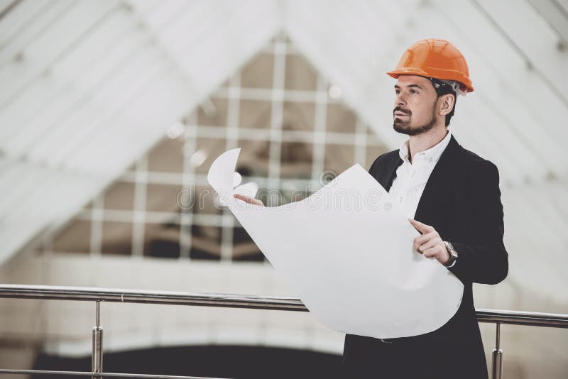 Fotoet av den manliga arkitekten i rött hardhatinnehav gör en skiss av royaltyfri fotografi Fotoet av den manliga arkitekten i rött hardhatinnehav gör en skiss av royaltyfri fotografi