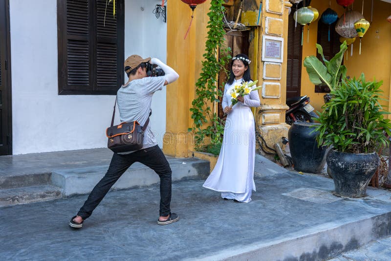 Fotografa vietnamita fotografa una ragazza con un bouquet di fiori vicino al vecchio muro giallo a hoi e in una città vietnam fotografie stock libere da diritti