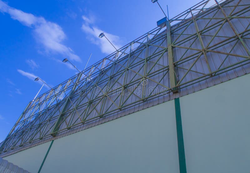 The large green steel billboard frame is located on the metal sheet roof in front of the factory under the blue sky and clouds. The large green steel billboard frame is located on the metal sheet roof in front of the factory under the blue sky and clouds