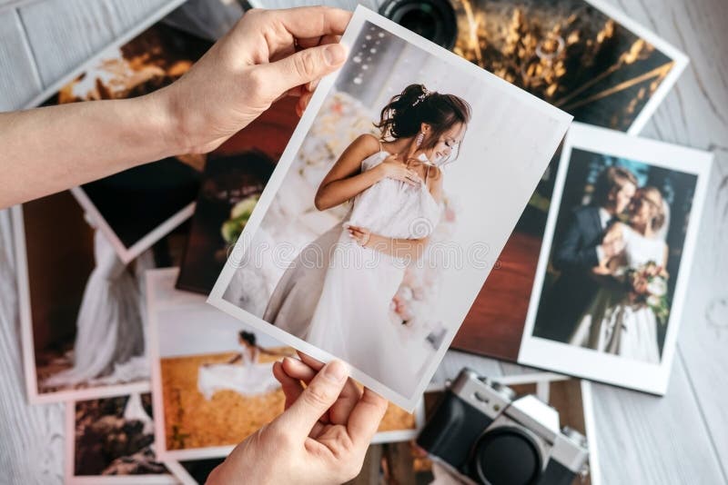 Fotos impressas do casamento com os noivos, uma câmera do preto do vintage e mãos da mulher com foto foto de stock Fotos impressas do casamento com os noivos, uma câmera do preto do vintage e mãos da mulher com foto foto de stock
