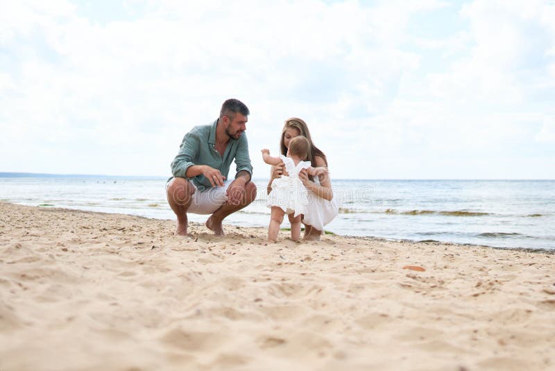 Fotosesja szczęśliwych rodziców bawiących się z 1-letnią dziewczynką grającą na piaszczystej plaży zdjęcie stock