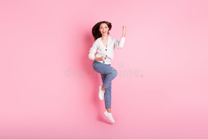 Fotot i full storlek av glad entusiastisk ung kvinna som hoppar upp i luften och höjer filtret som vinns isolerade på den rosa bak fotografering för bildbyråer