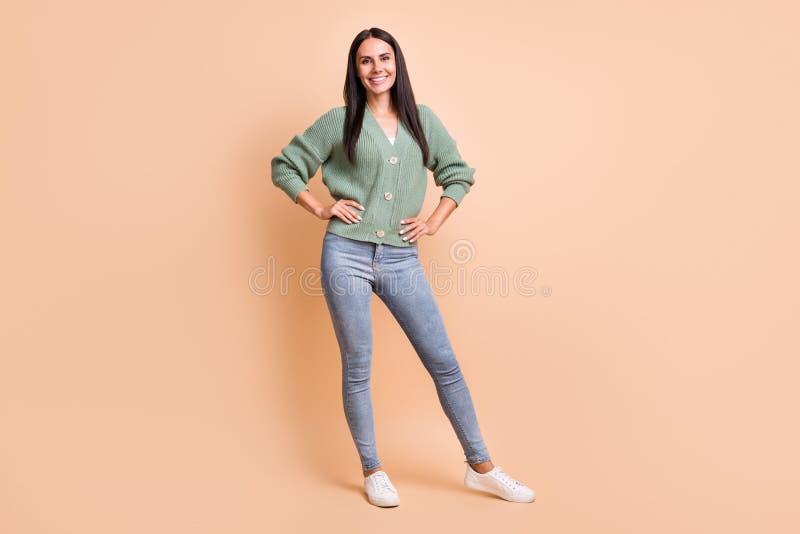 Fotot med full längd på en positiv, glad kvinna som håller hand och som bär gröna smycken som isolerats på beige färgbakgrund royaltyfri bild