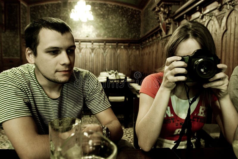 Man and woman sitting in a restaurant, the woman has a camera positioned in front of her face to shoot. Intentional noise. Man and woman sitting in a restaurant, the woman has a camera positioned in front of her face to shoot. Intentional noise.