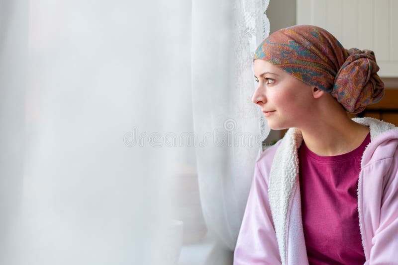 Foulard d'uso ed accappatoio del giovane malato di cancro della femmina adulta che si siedono nella cucina