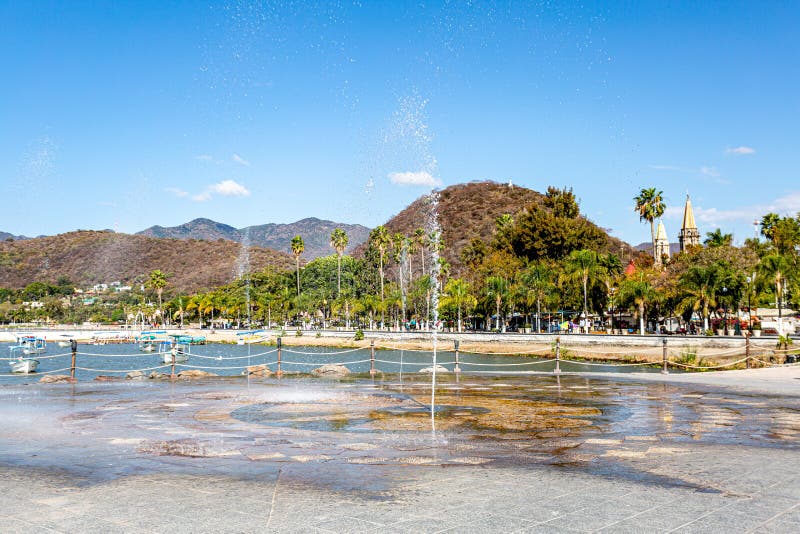 Fountain spraying the ground with jets of water on the promenade of Lake Chapalah the town in the background, sunny day with a