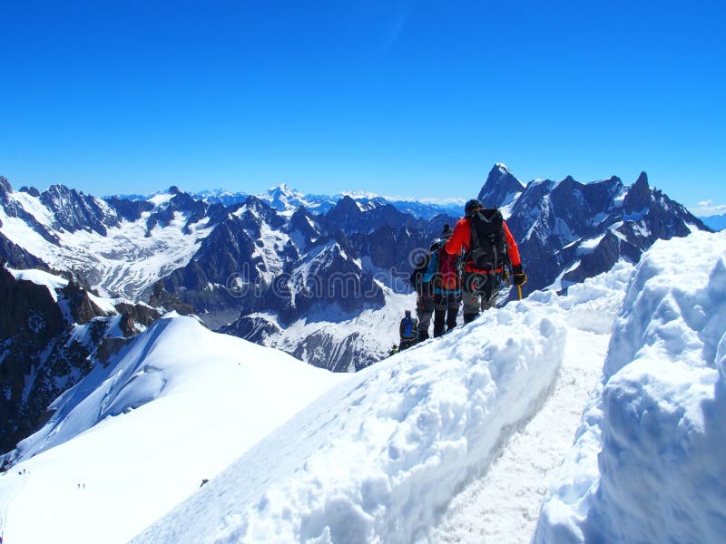 Four alpinists and mountaineer climbers in french Alps and high alpine mountains range with clear blue sky in warm and sunny summer day: AIGUILLE DU MIDI, CHAMONIX MONT BLANC / FRANCE – JULY 2016. Four alpinists and mountaineer climbers in french Alps and high alpine mountains range with clear blue sky in warm and sunny summer day: AIGUILLE DU MIDI, CHAMONIX MONT BLANC / FRANCE – JULY 2016.