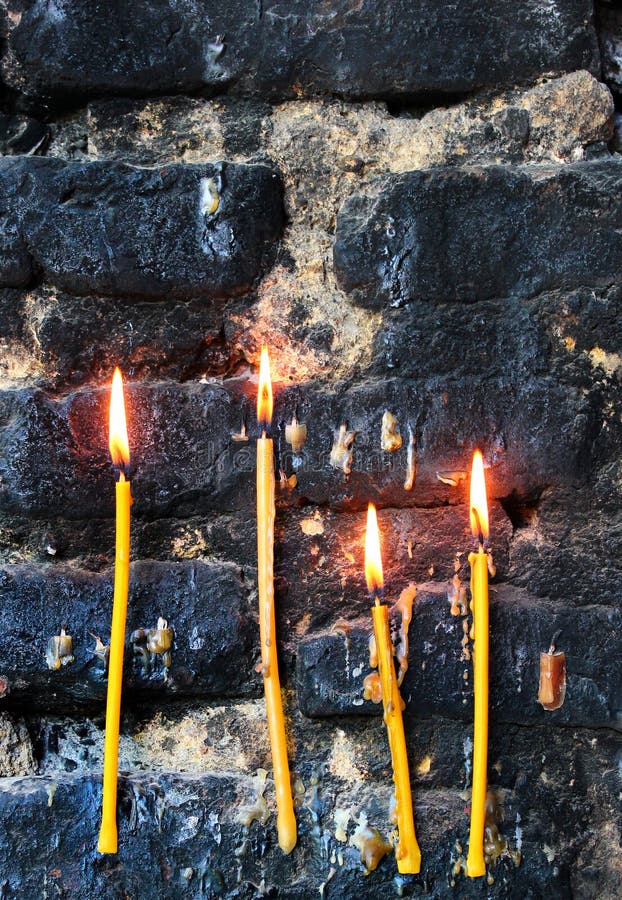 Four Burning Candles on Old Sooty Blackened Stone Wall Stock Image