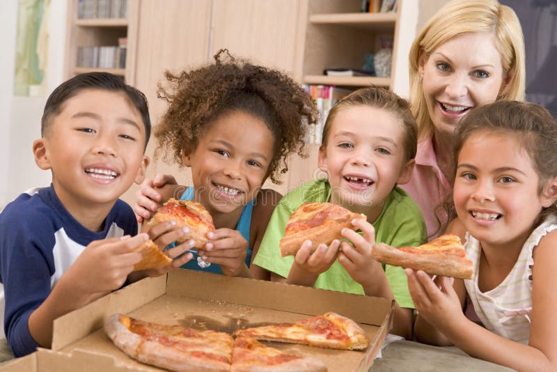 Quattro bambini piccoli in casa con la donna di mangiare la pizza.