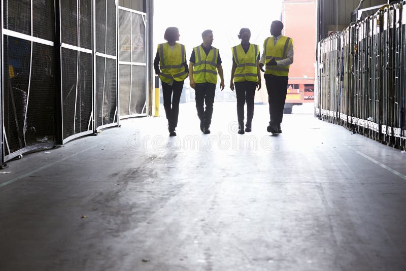 Four Colleagues in Reflective Vests Walking into a Warehouse Stock