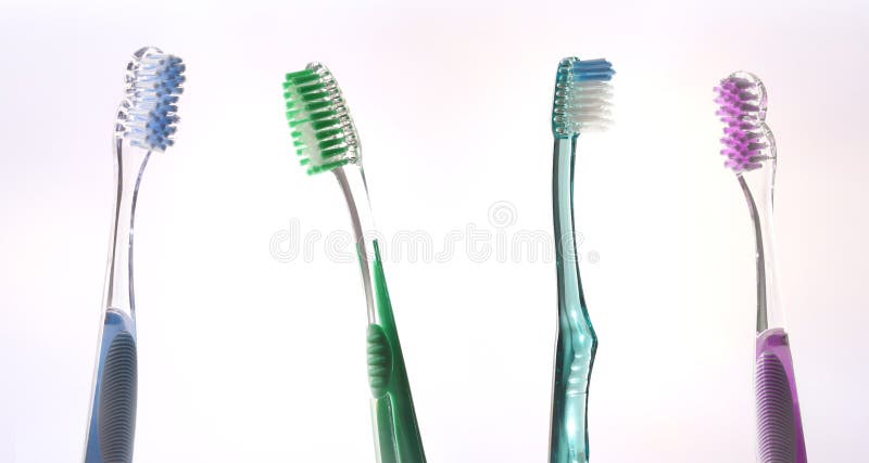 Four colorful transparent tooth brushes on pink gradient royalty free stock image
