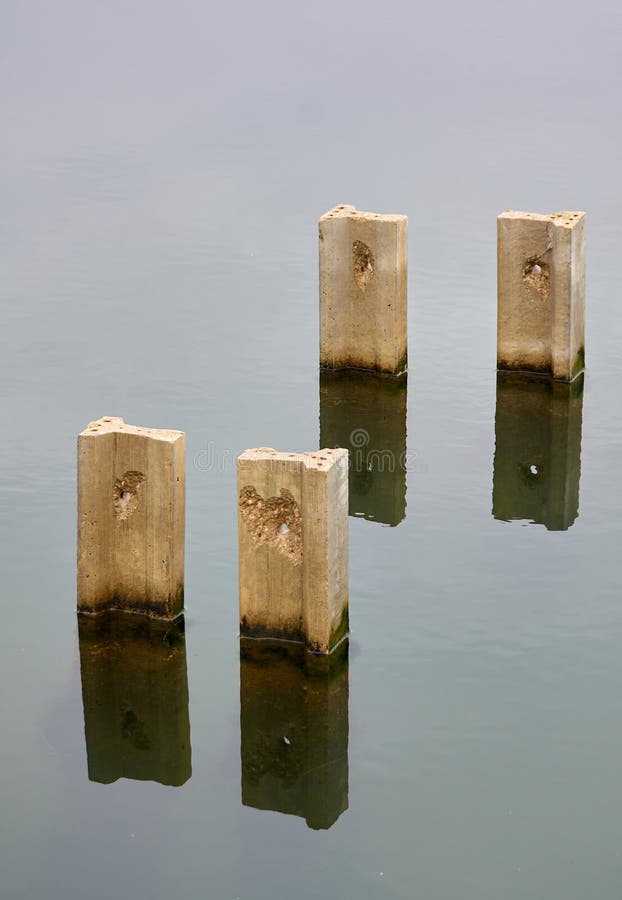 Four Concrete Pillars Submerged and Reflected in the Water Stock Photo